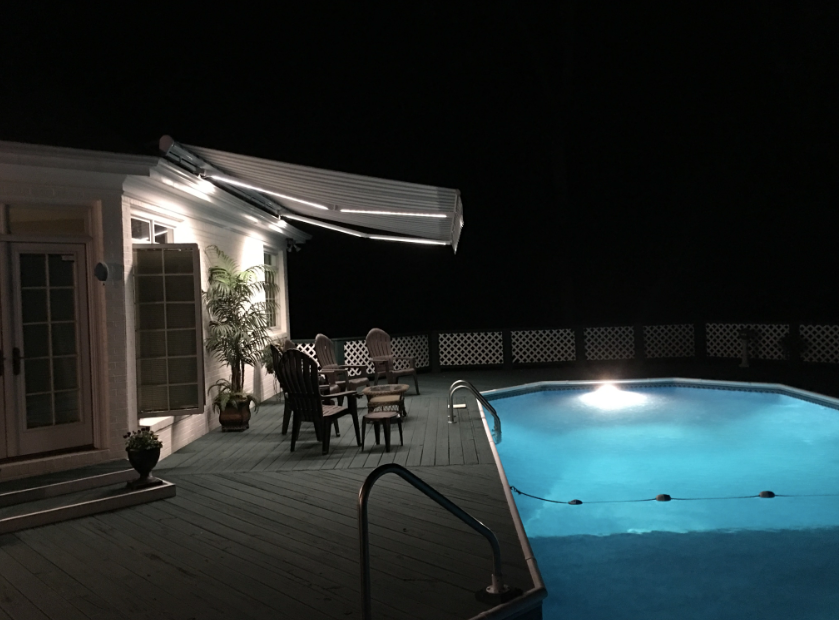 A swimming pool is lit up at night in front of a house.