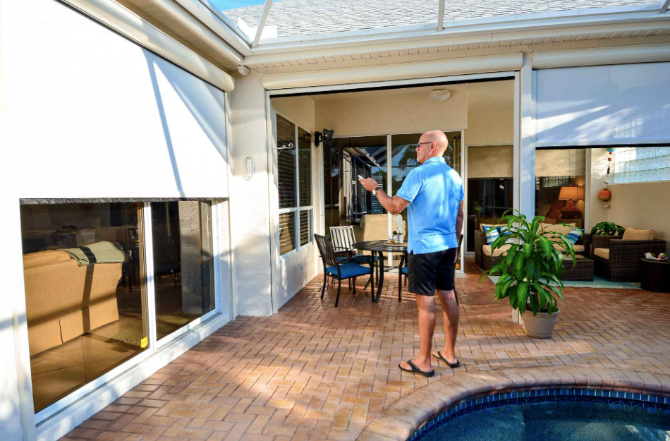 A man is standing on a patio next to a pool holding a remote control.