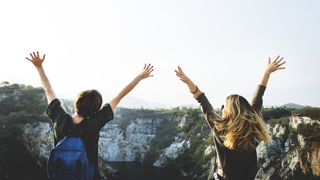 two women on mountain top raising their arms because managing summertime anxiety
