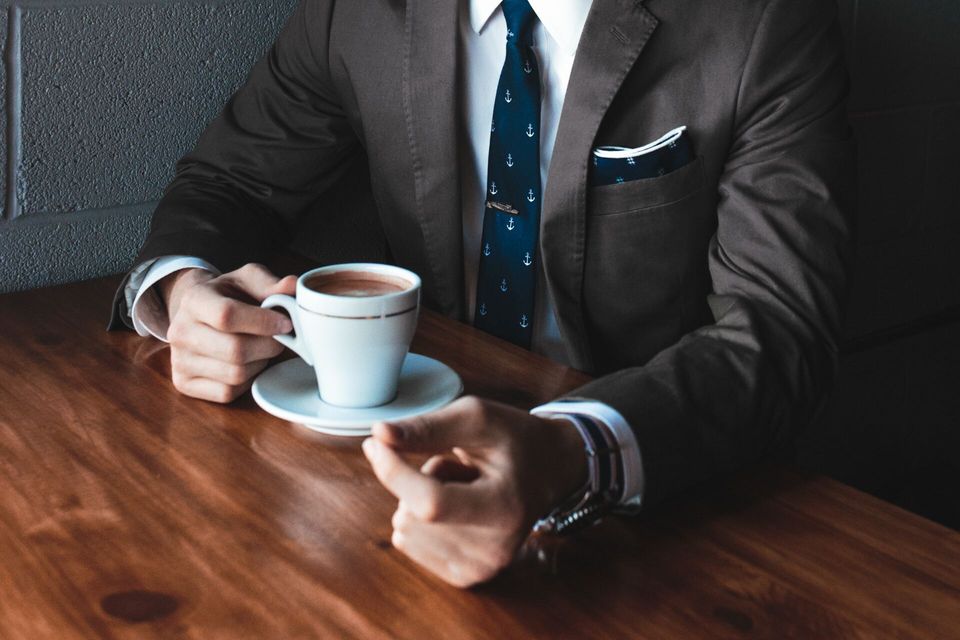 professional man in suit sitting at table with cup of coffee feeling in control