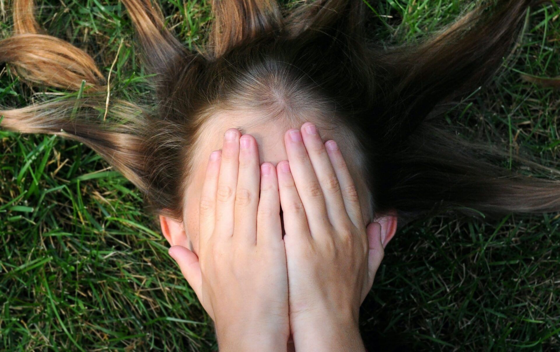woman lying on grass and covering her face because she's overwhelmed