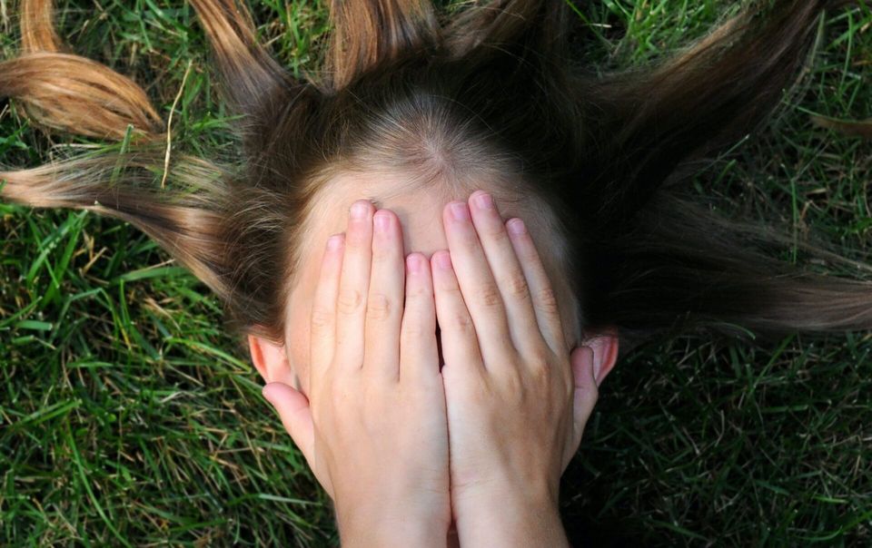 young woman lying on grass covering her face with her hands because mindset is fixed