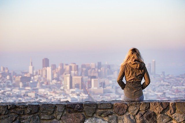 woman sitting on stone wall overlooking city trying to take more risks to overcome anxiety while on vacation