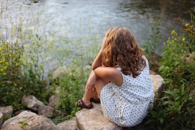girl sitting on a rock by a lake because anxiety got worse during summer