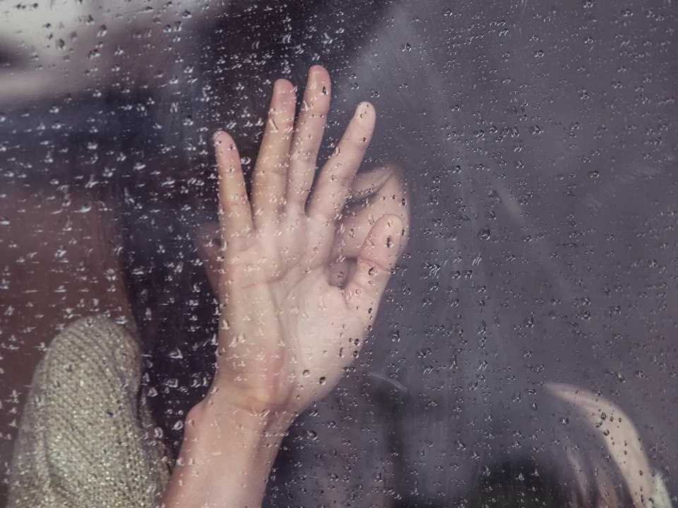 woman's head leaning on her hand against glass with rain on it for anxiety about life events