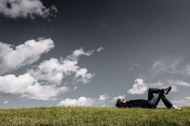 man lying on grass looking at sky spending time alone to manage anxiety of being away from home