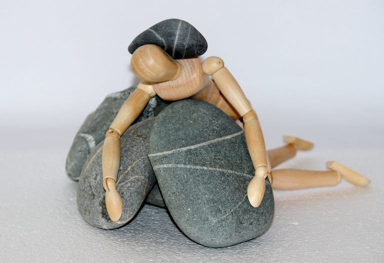 wooden figurine of human trapped between rocks because of cost of using insurance