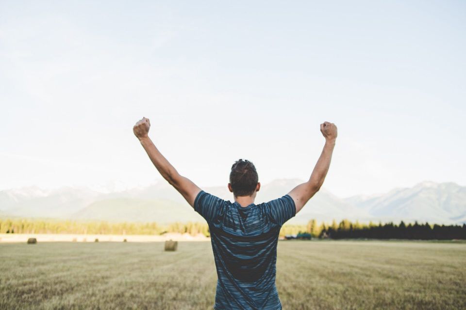 man standing in field holding his arms up with mindset for success