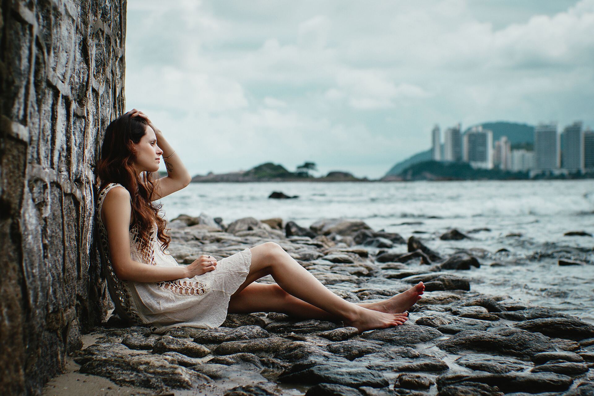 Woman leaning against rock wall by the beach thinking about OCD symptoms
