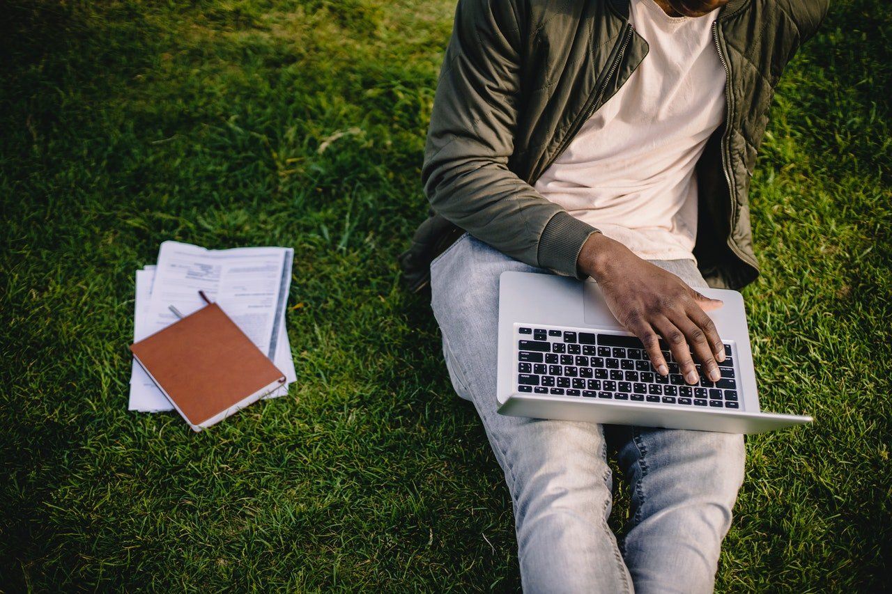 man on grass looking on laptop for online mental health resources