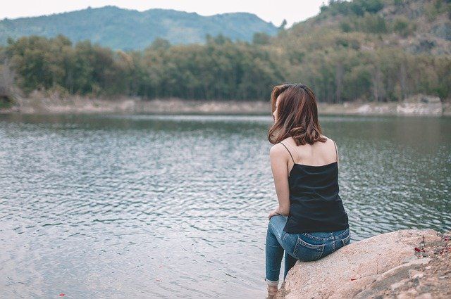 woman on a rock looking at lake out of shame and anxiety of BFRB