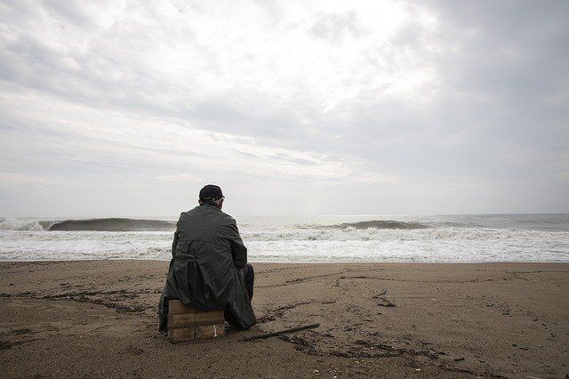 old man sitting on crate on beach looking at ocean because anxious and depressed