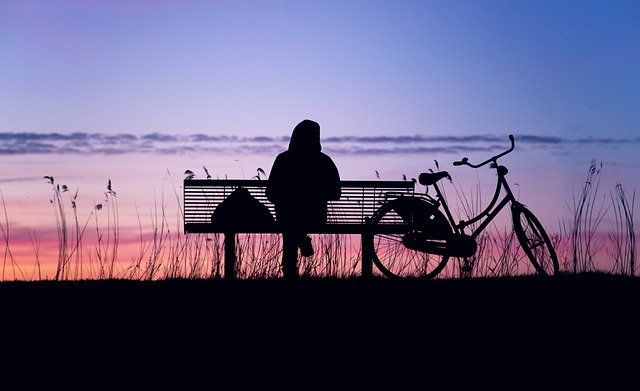 person sitting alone on bench during sunset for risk factors for why successful people are at risk for suicide