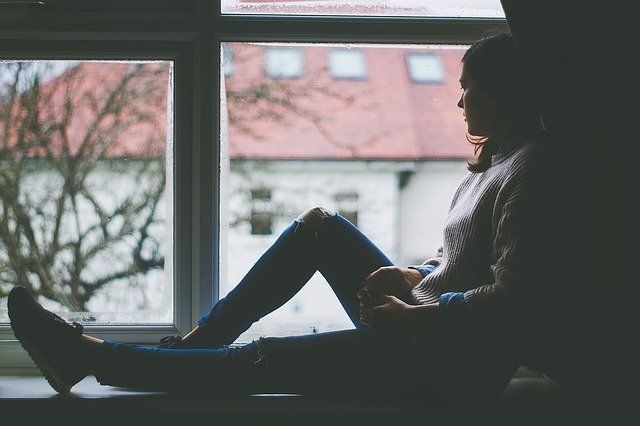 woman sitting on window sill staring outside because of depression and anxiety