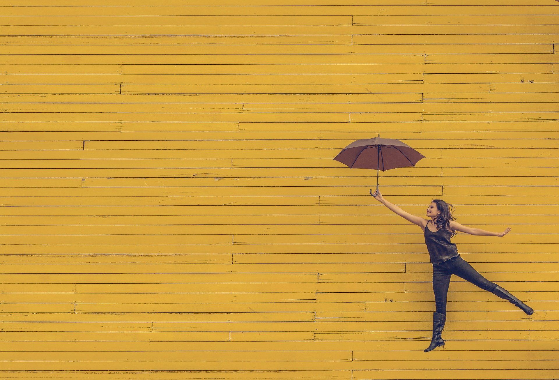 woman holding red umbrella while jumping in front of yellow wall for next steps for managing anxiety