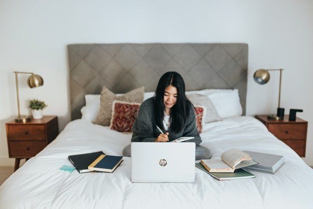 woman sitting on bed with laptop and books making self care hard