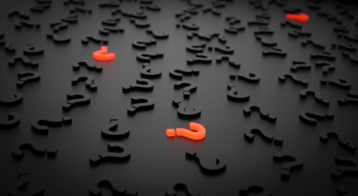 A red question mark is surrounded by black letters on a black surface.