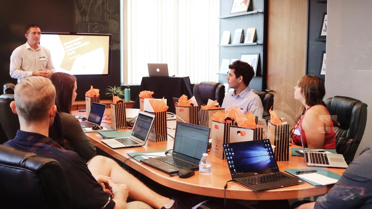 A group of people are sitting around a table with laptops in a conference room.