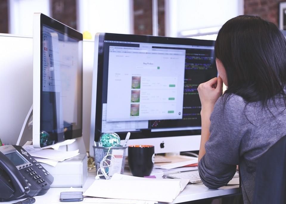 A woman is sitting at a desk looking at a computer screen.