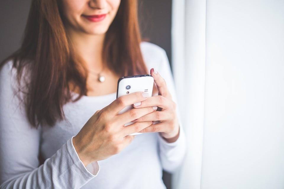 A woman is holding a cell phone in her hands and looking at it.