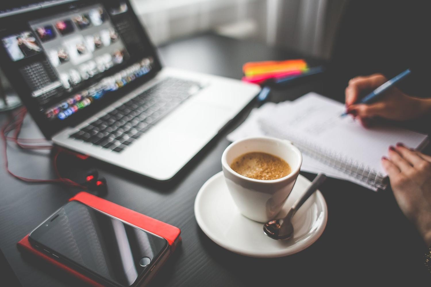 A person is writing in a notebook next to a cup of coffee