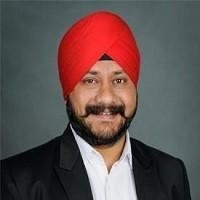 Harpreet Singh  wearing a red turban and a black suit is smiling.