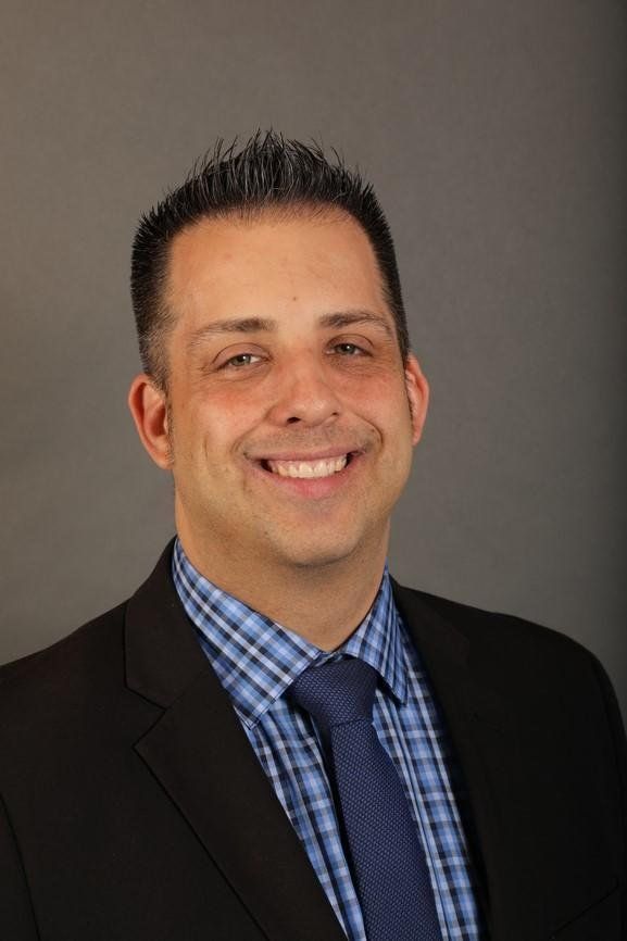 Matthew Victoria in a suit and tie is smiling for the camera.