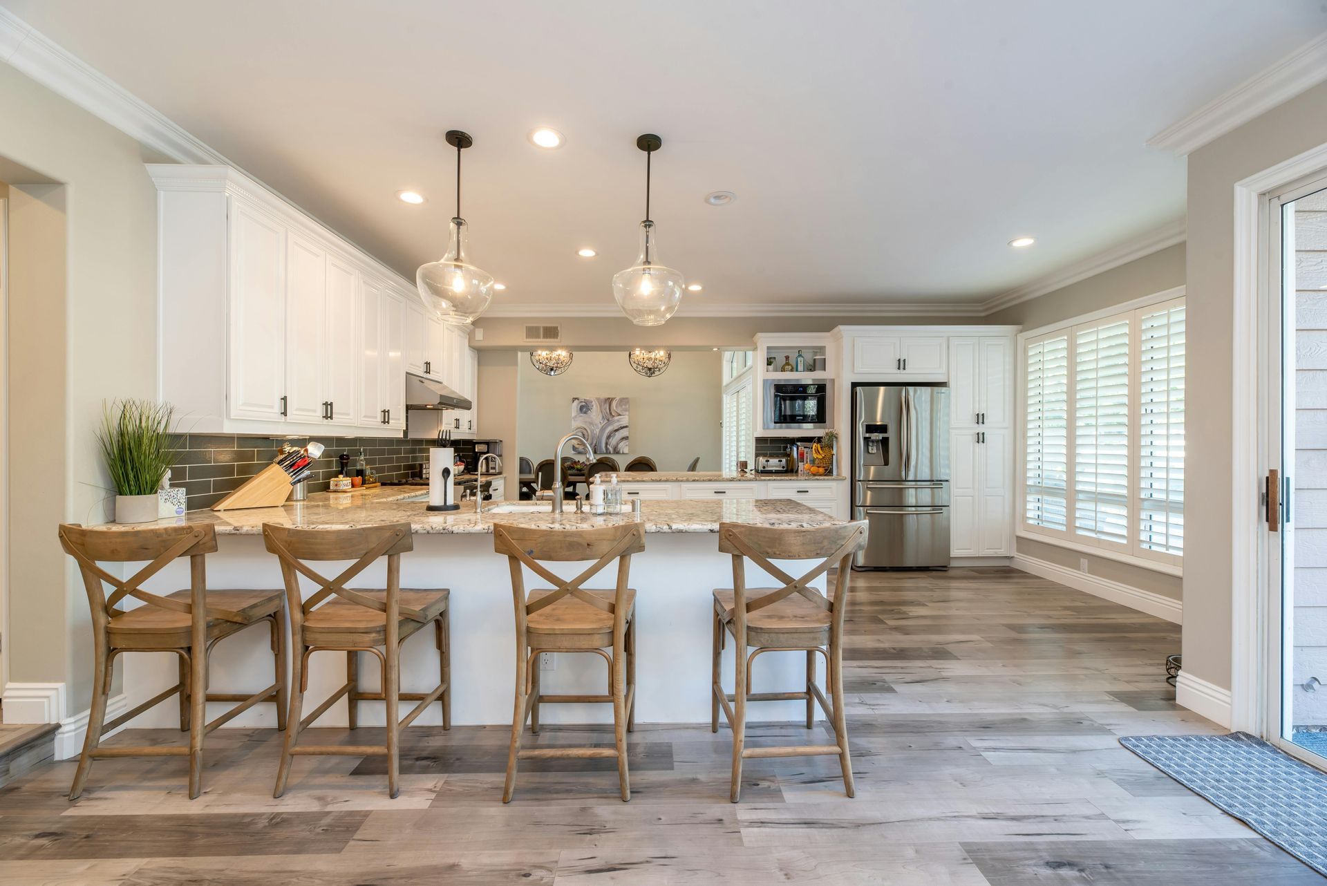 A kitchen with white cabinets , stainless steel appliances , wooden floors and a large island with chairs.