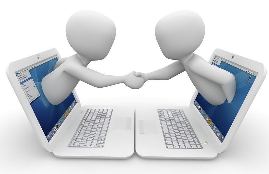 Two people shaking hands in front of two laptops