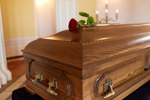 Wooden coffin with a red rose, viewed indoors in a softly lit funeral setting