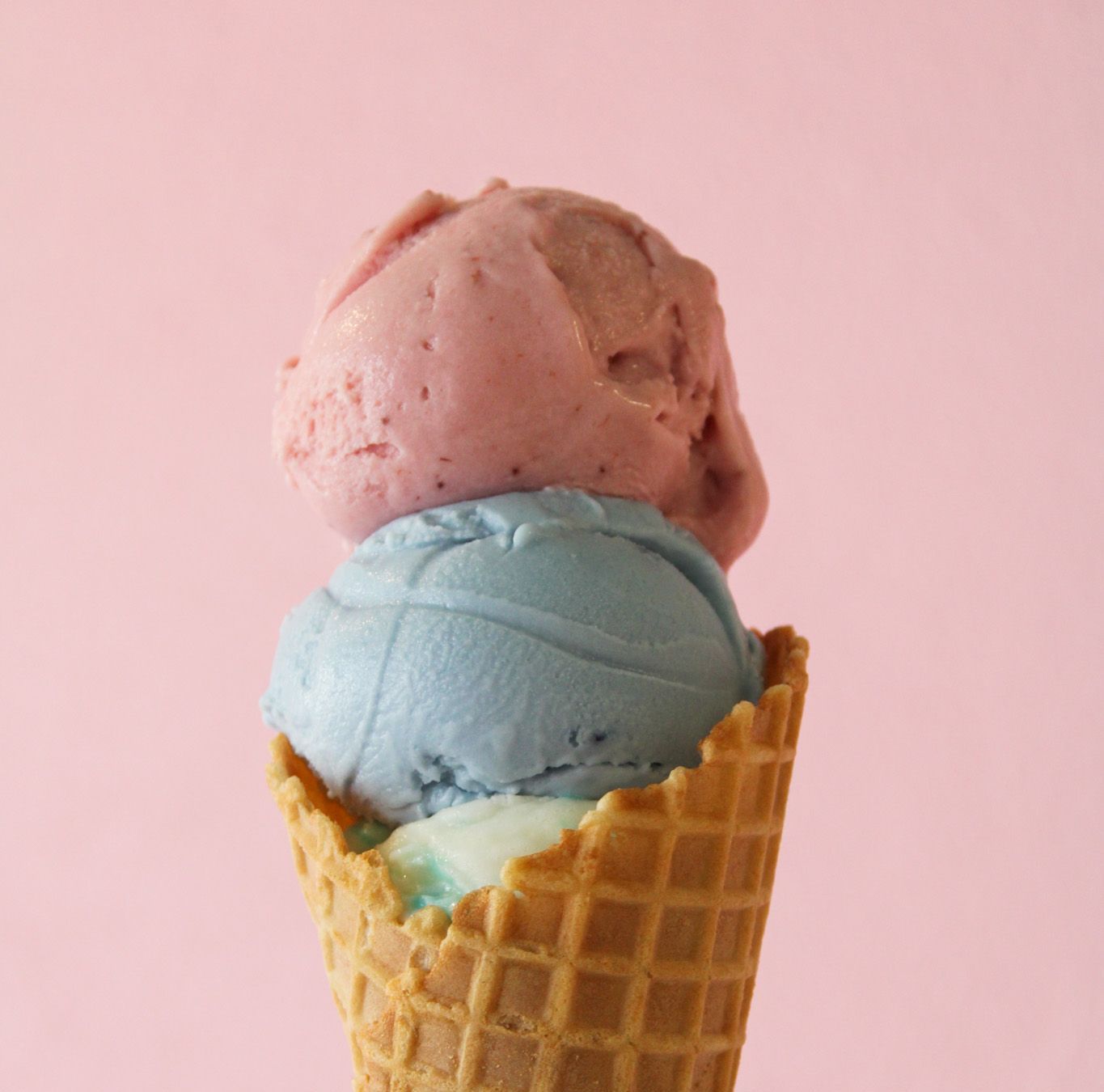 Two scoops of ice cream in a waffle cone on a pink background