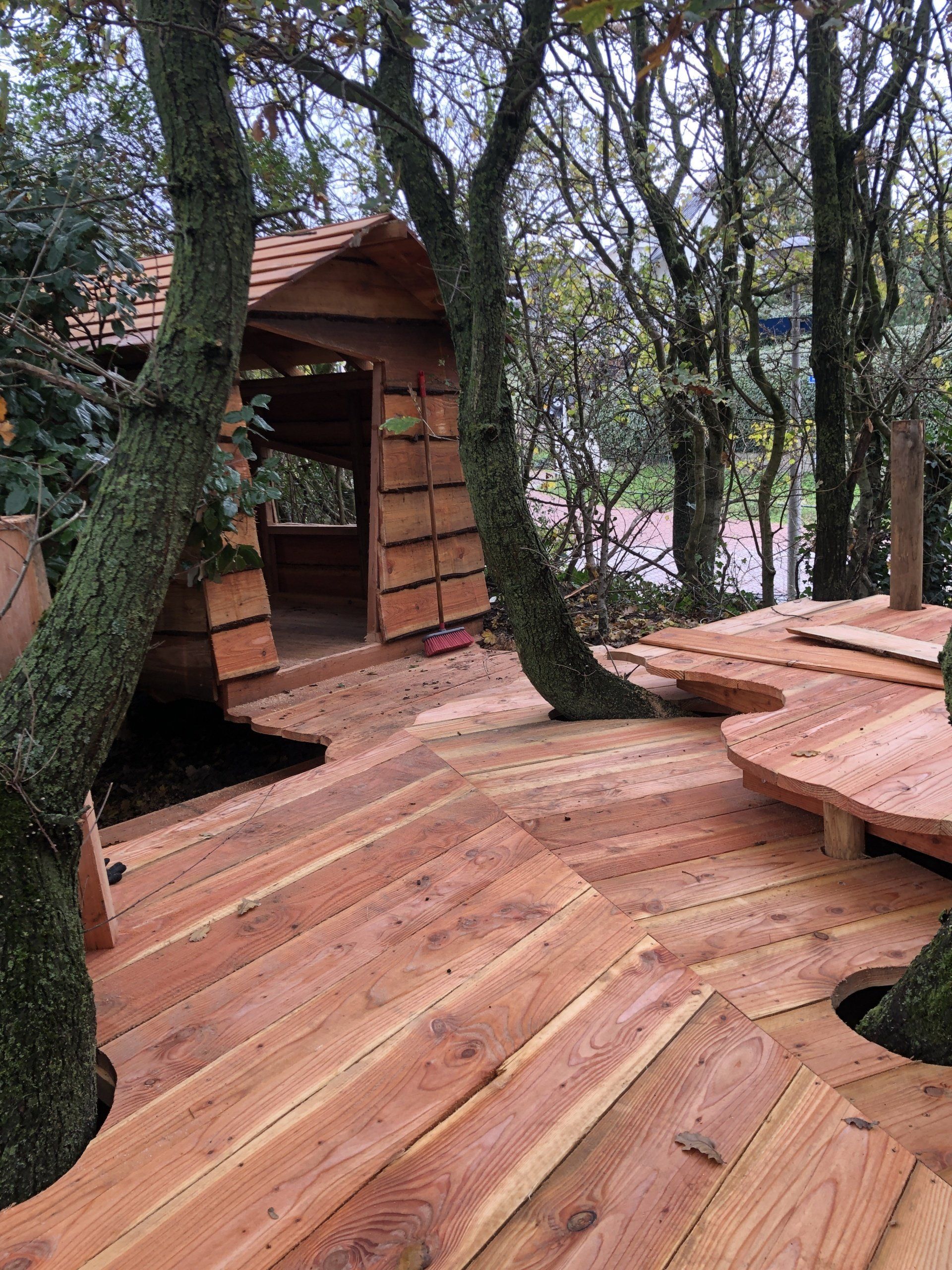 Een houten terras met een boomhut op de achtergrond.