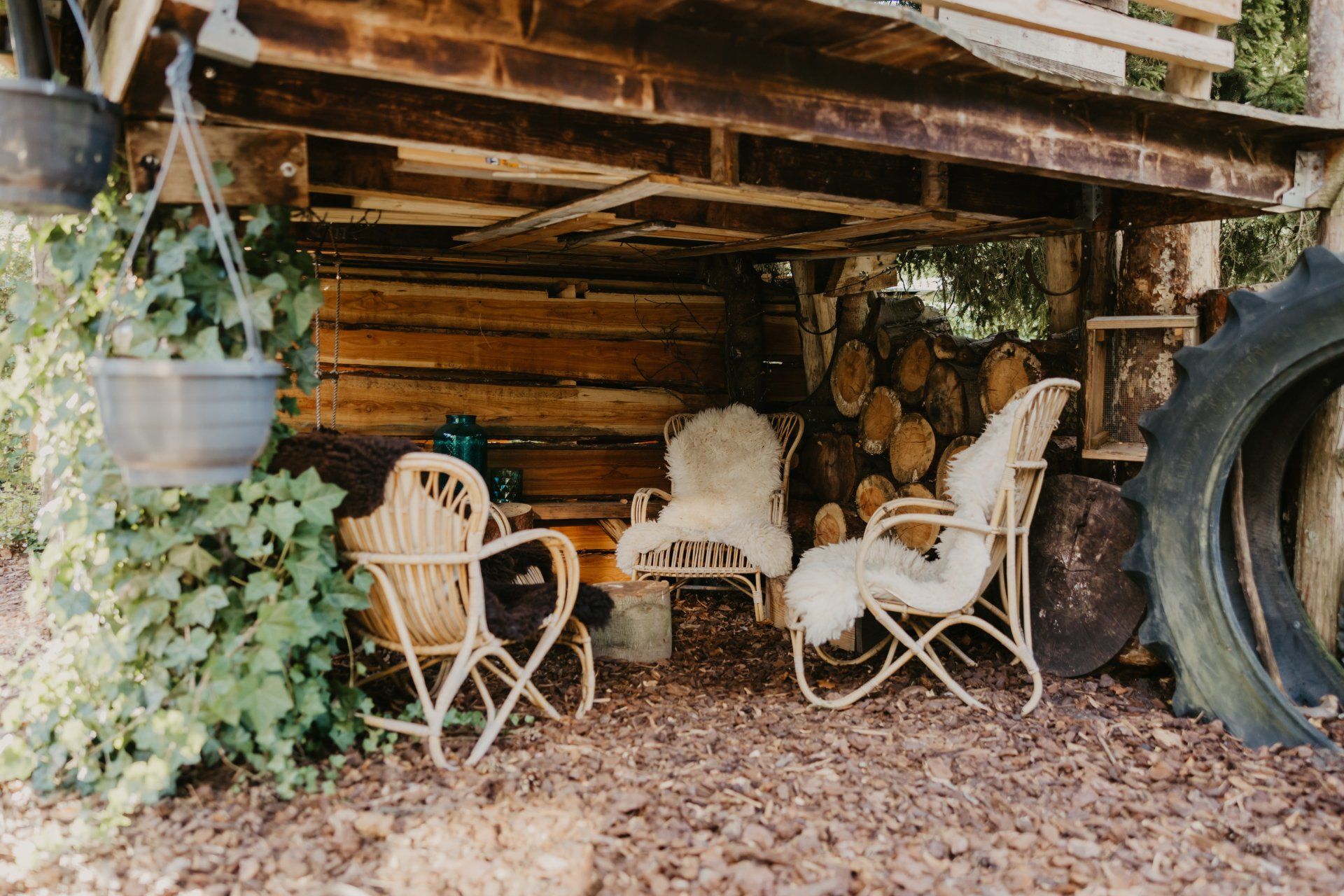 Een houten schuurtje met stoelen en een autoband ervoor.