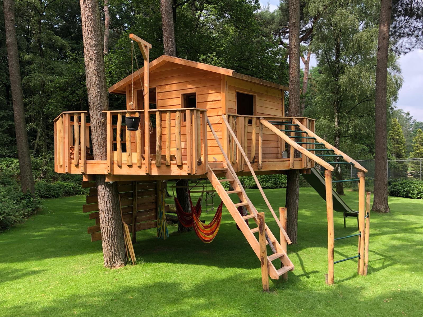 Een houten boomhut staat bovenop een weelderig groen gazon.