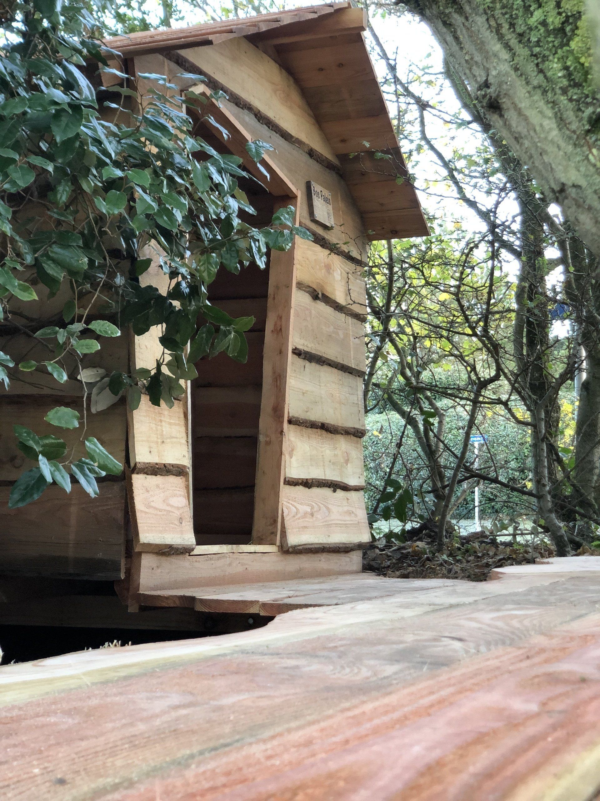Een klein houten huis staat op een houten tafel in het bos.