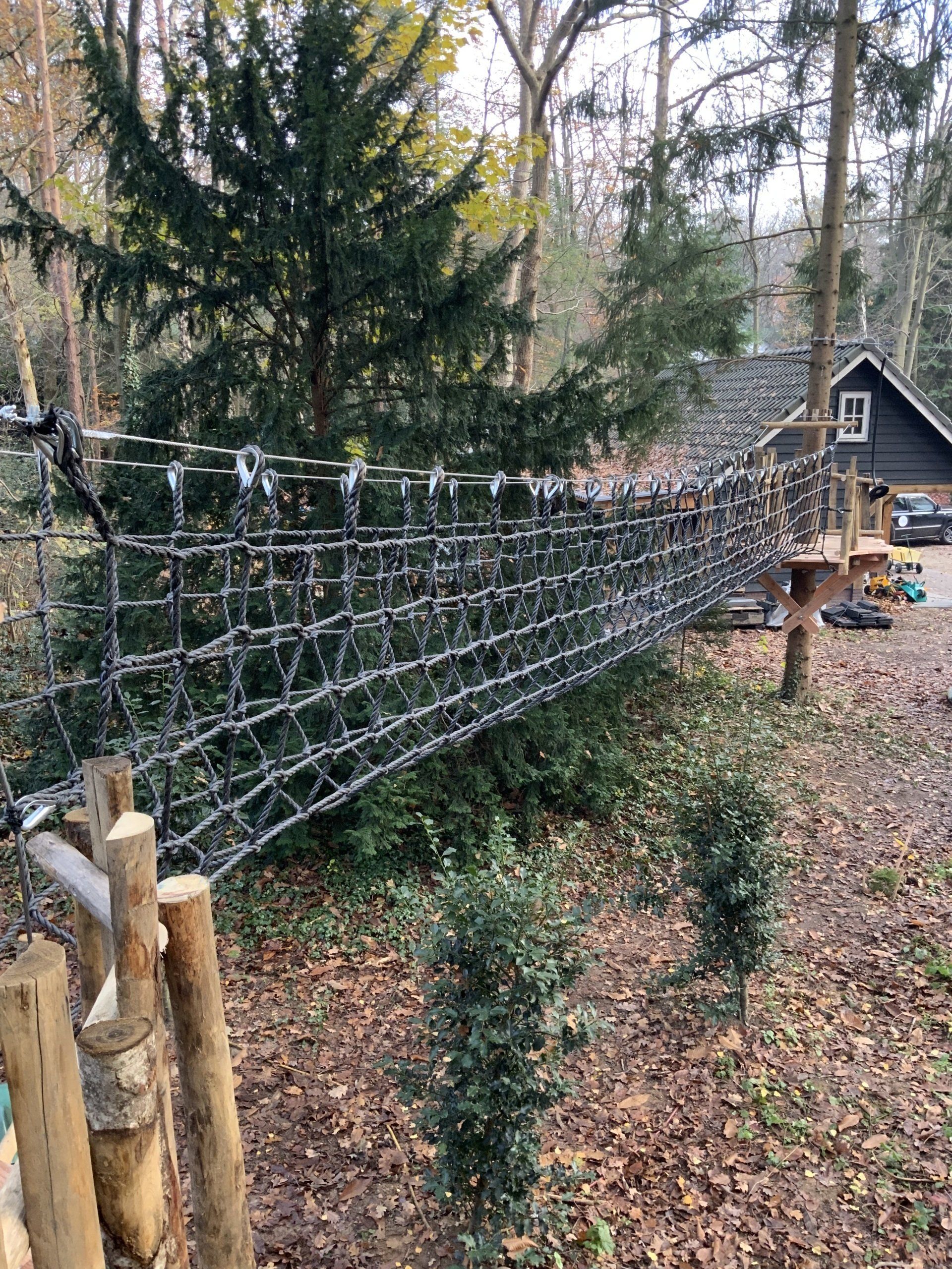 Midden in het bos ligt een touwbrug.