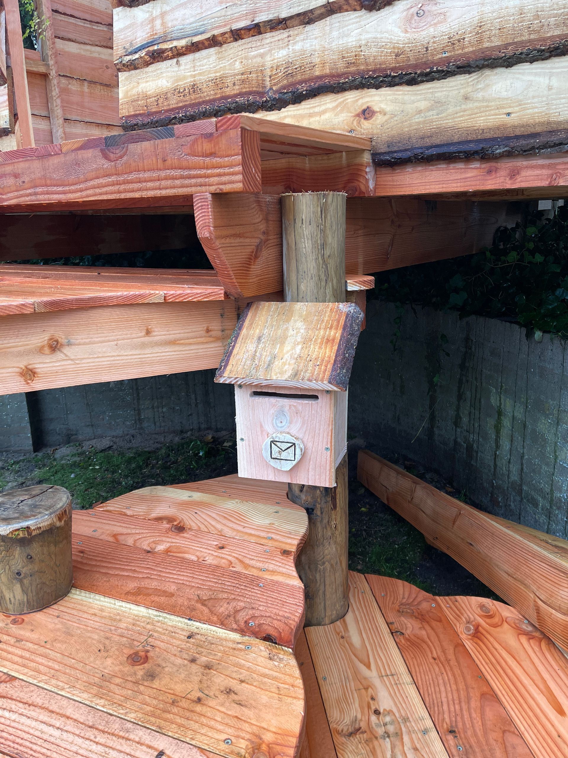 Bovenop een houten trap staat een houten brievenbus.