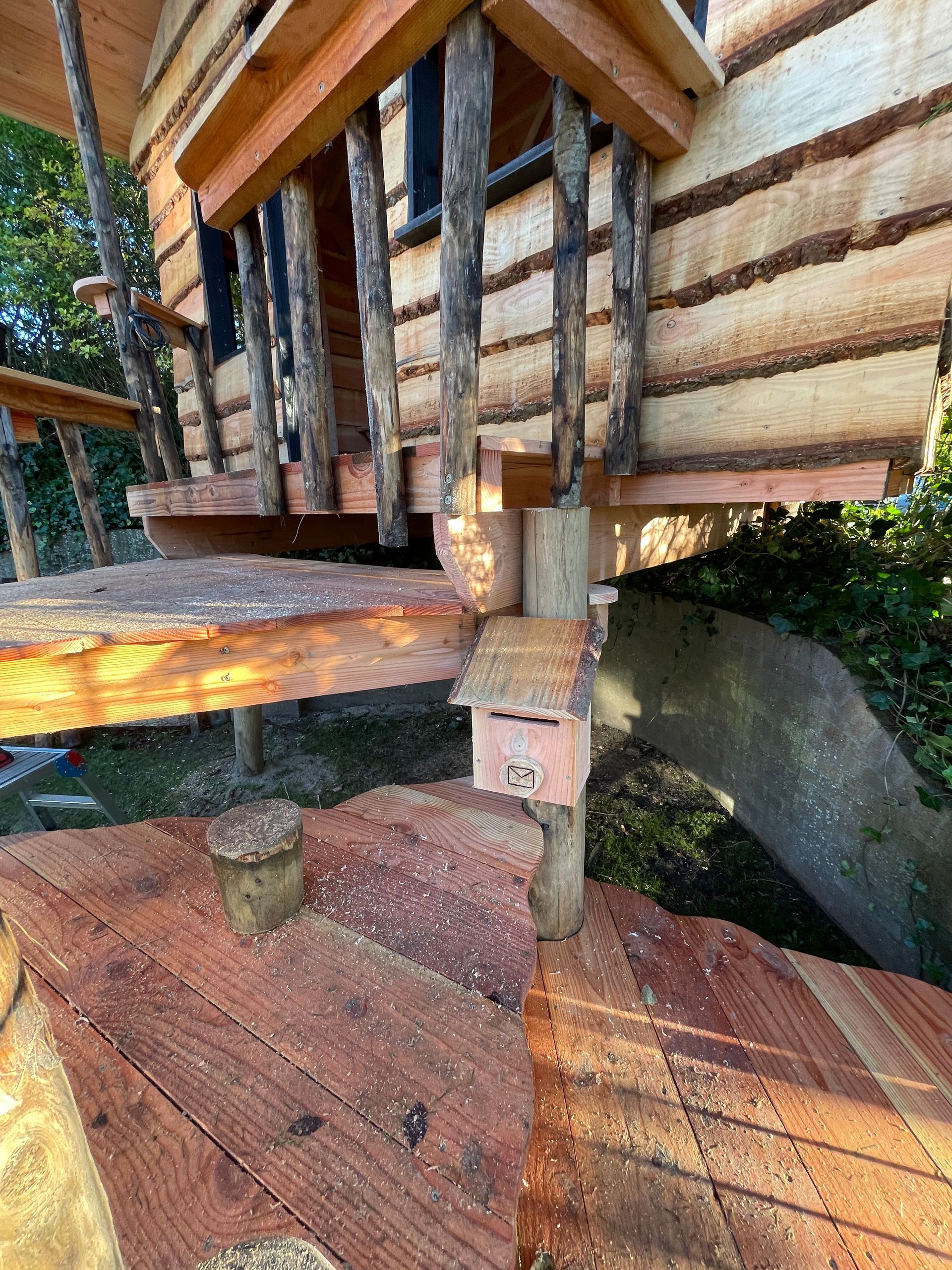 Een houten boomhut met trap en een brievenbus aan de zijkant.