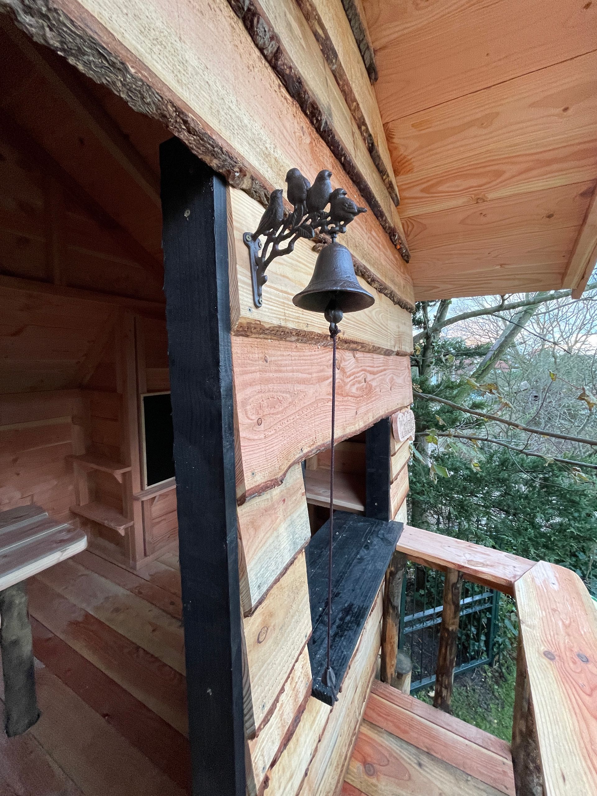 Een houten huis met een bel aan de zijkant.
