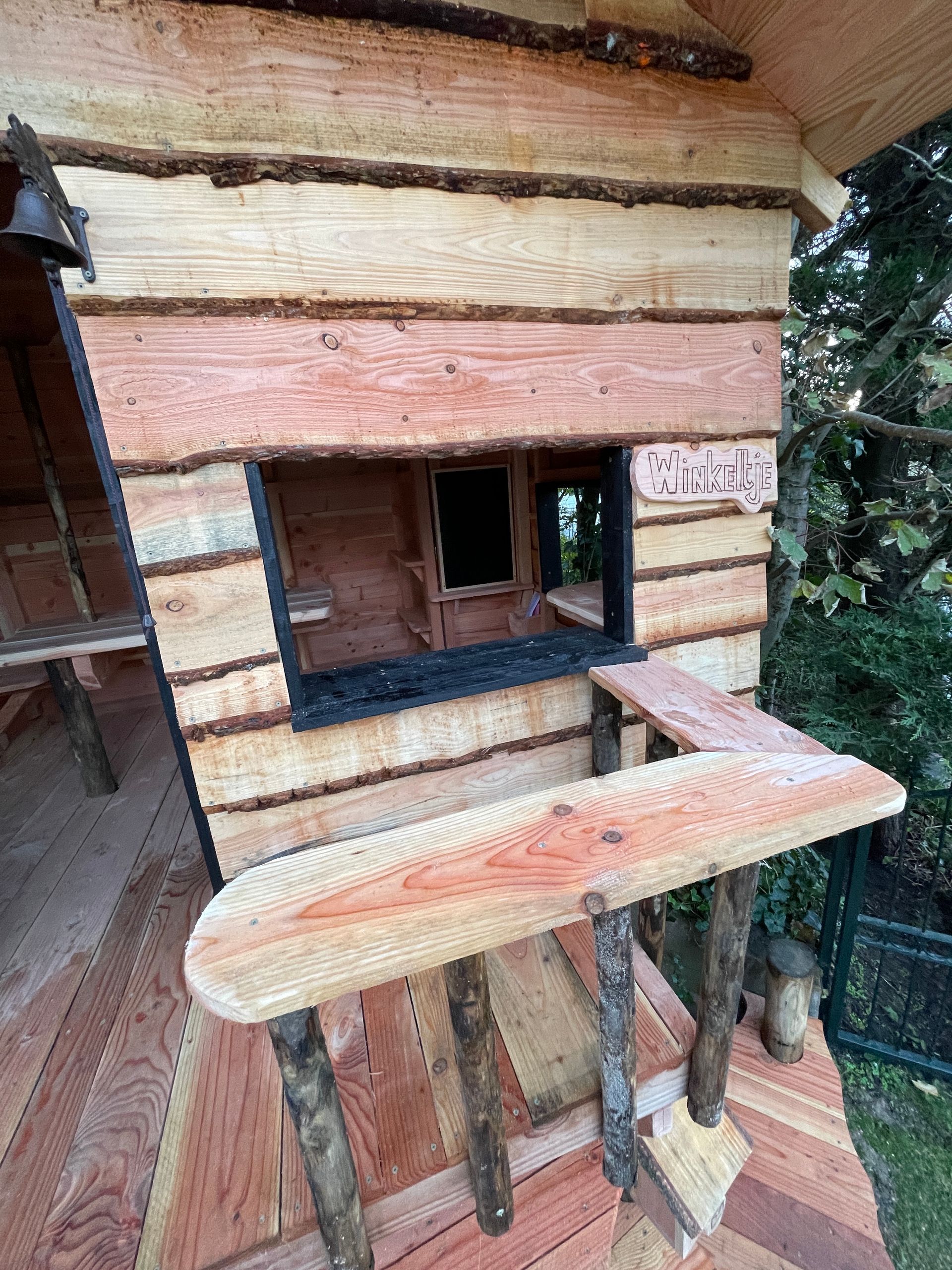 Een houten boomhut met trappen en een raam.