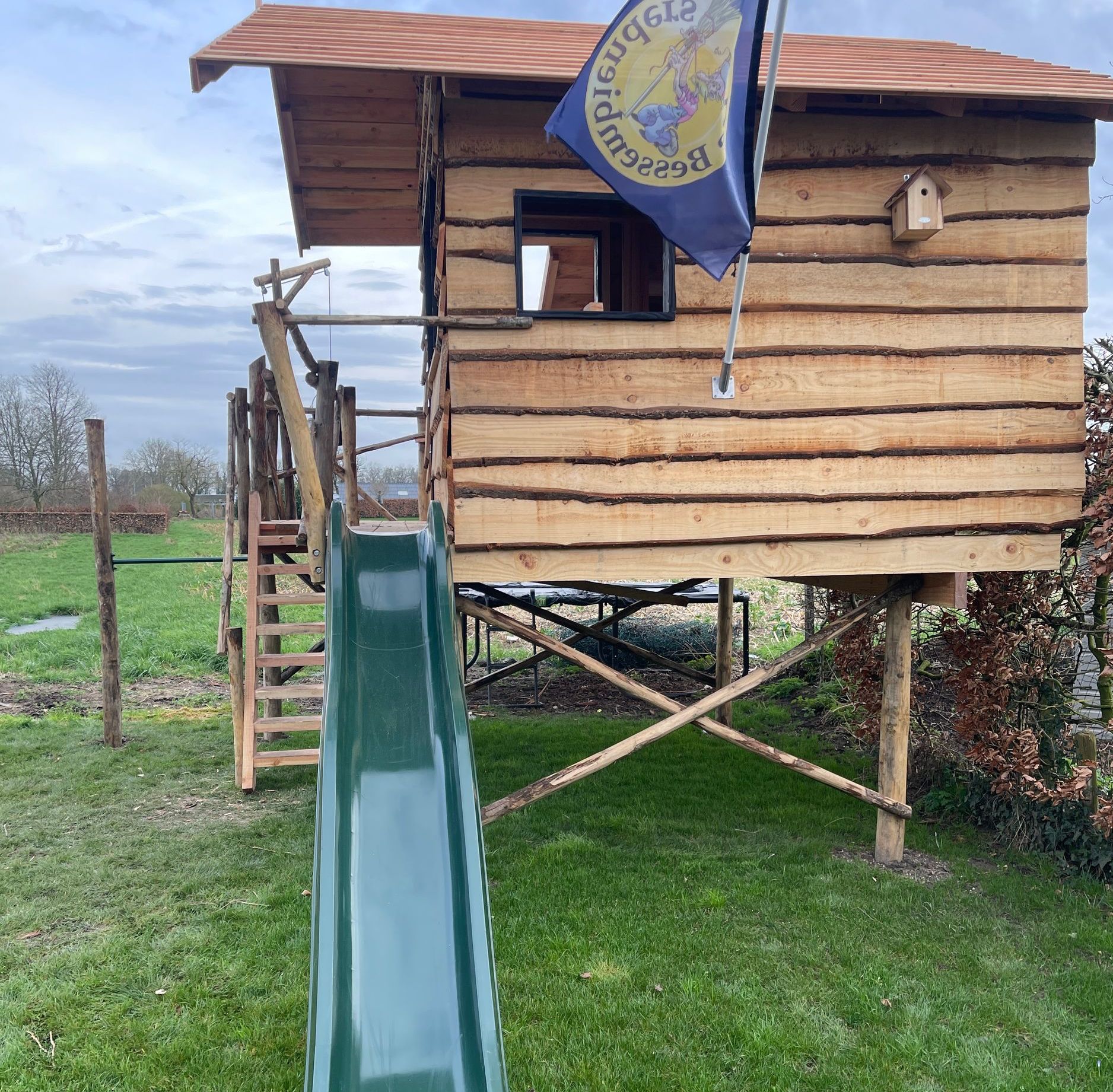 Een houten huis met een glijbaan en een vlag met de tekst 'vrijheid' erop
