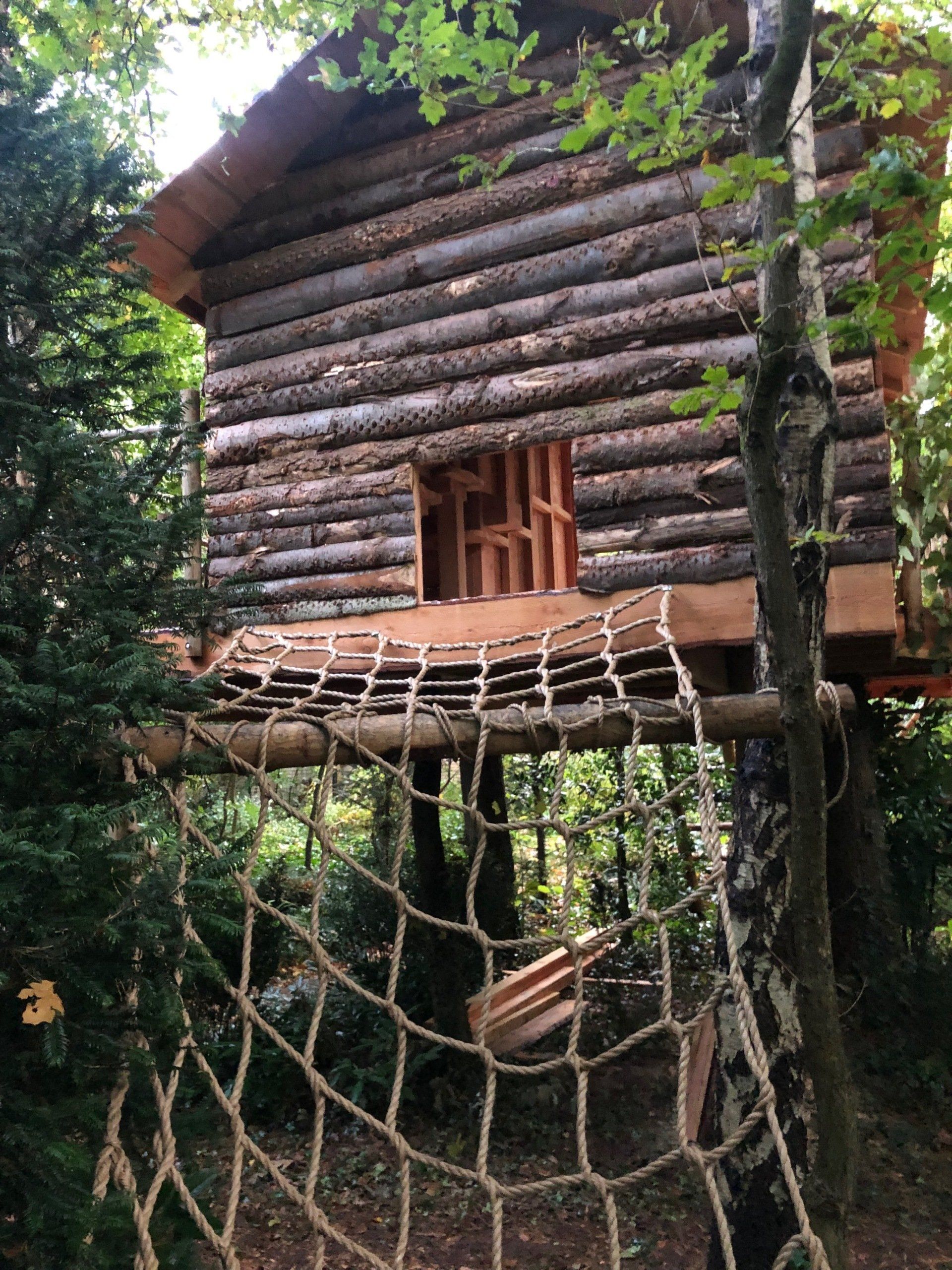Een houten boomhut met een touwbrug in het bos.