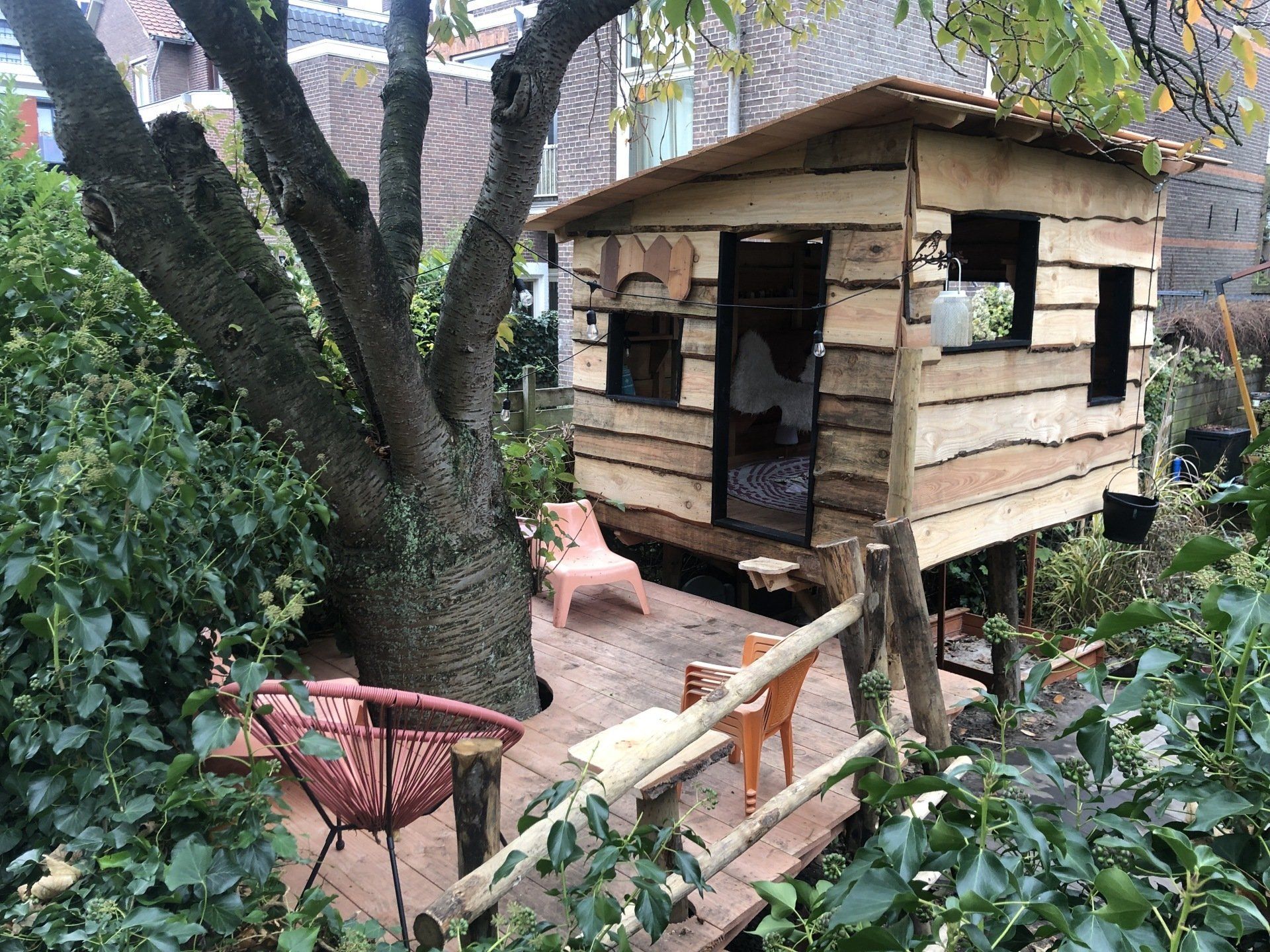 Een houten boomhut zit onder een boom in een tuin.