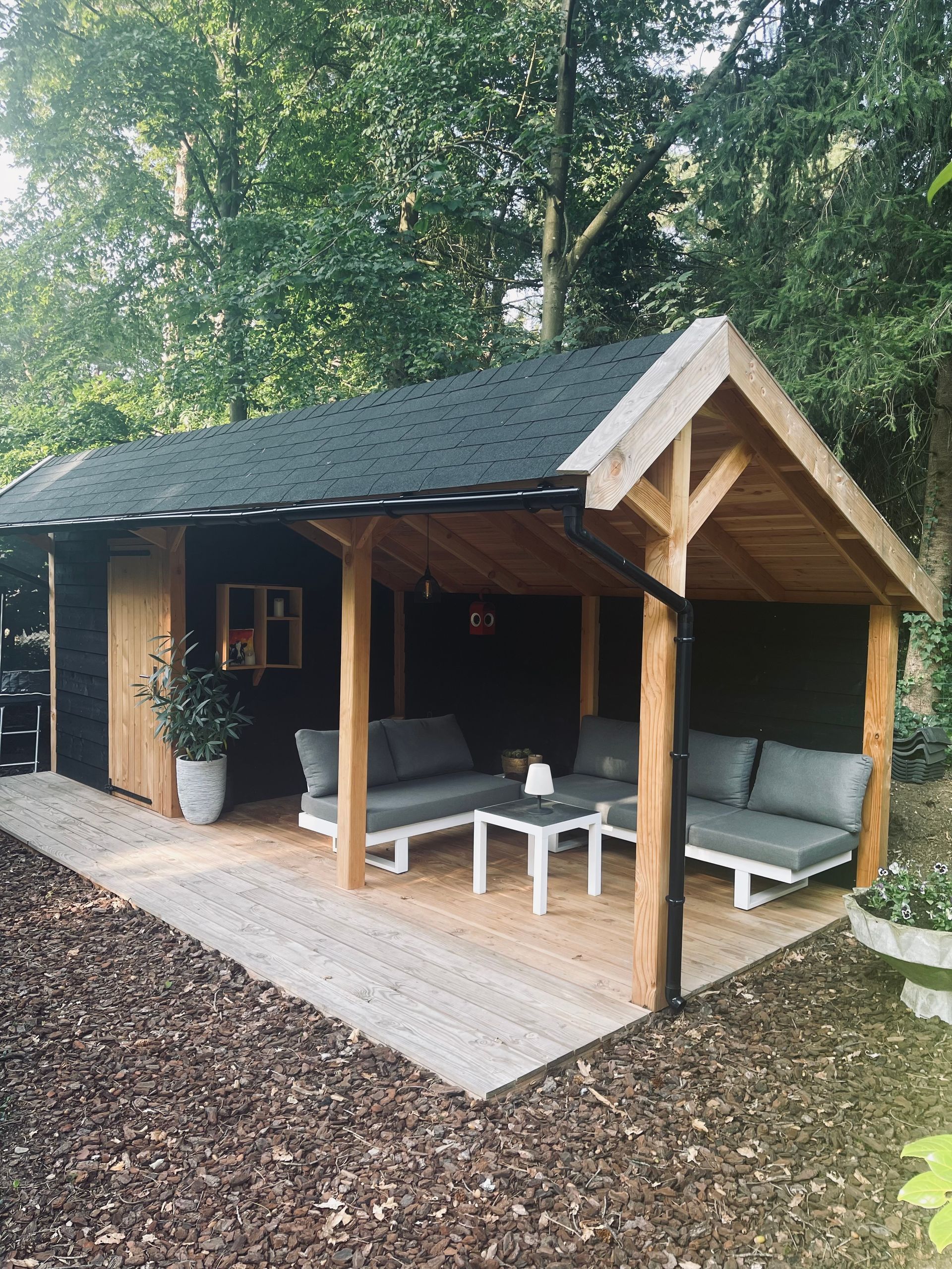 Een houten schuur met een overdekt terras en daaronder een bank en tafel.