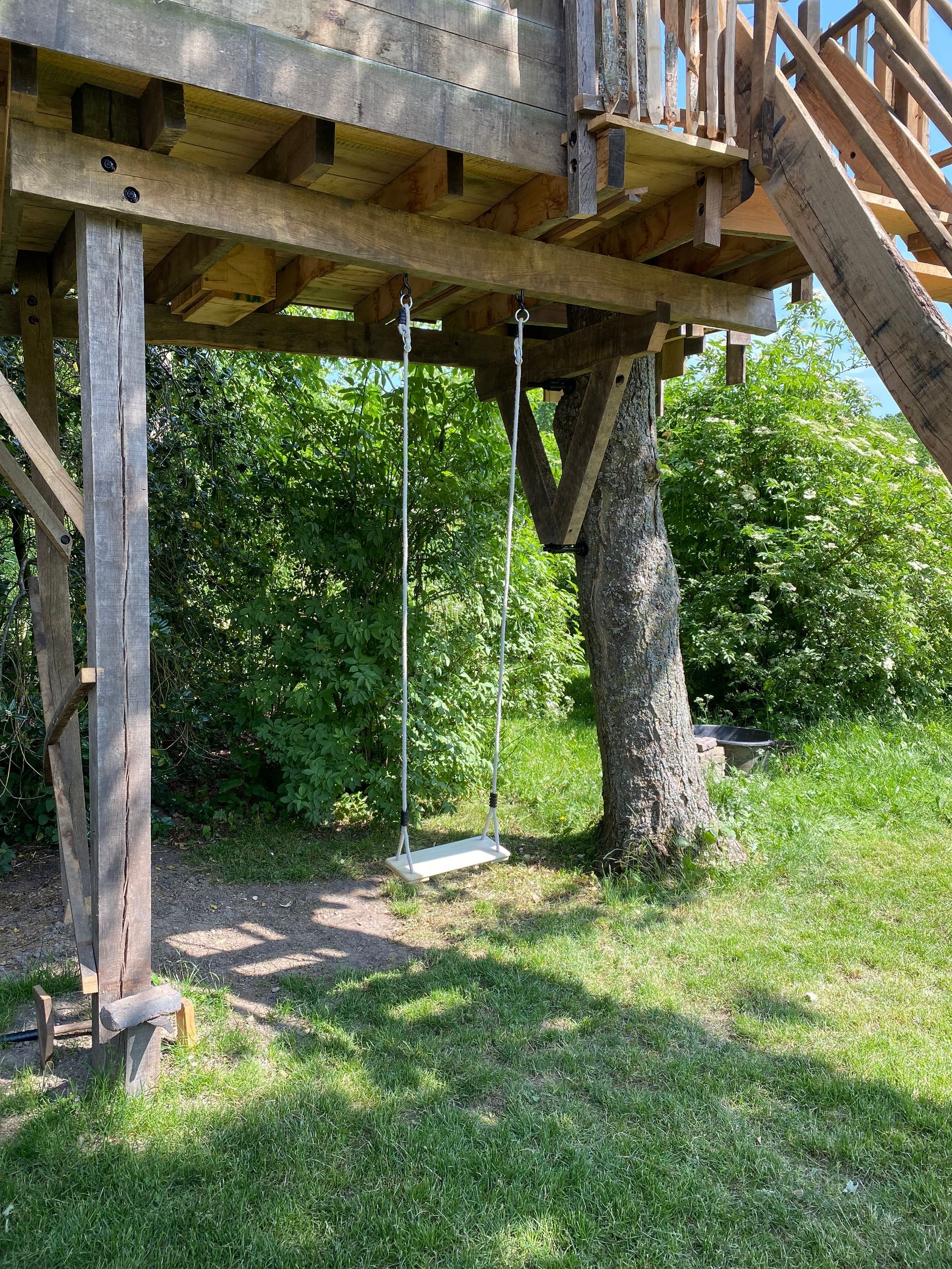 Een boomhut met een trap en een schommel eronder.