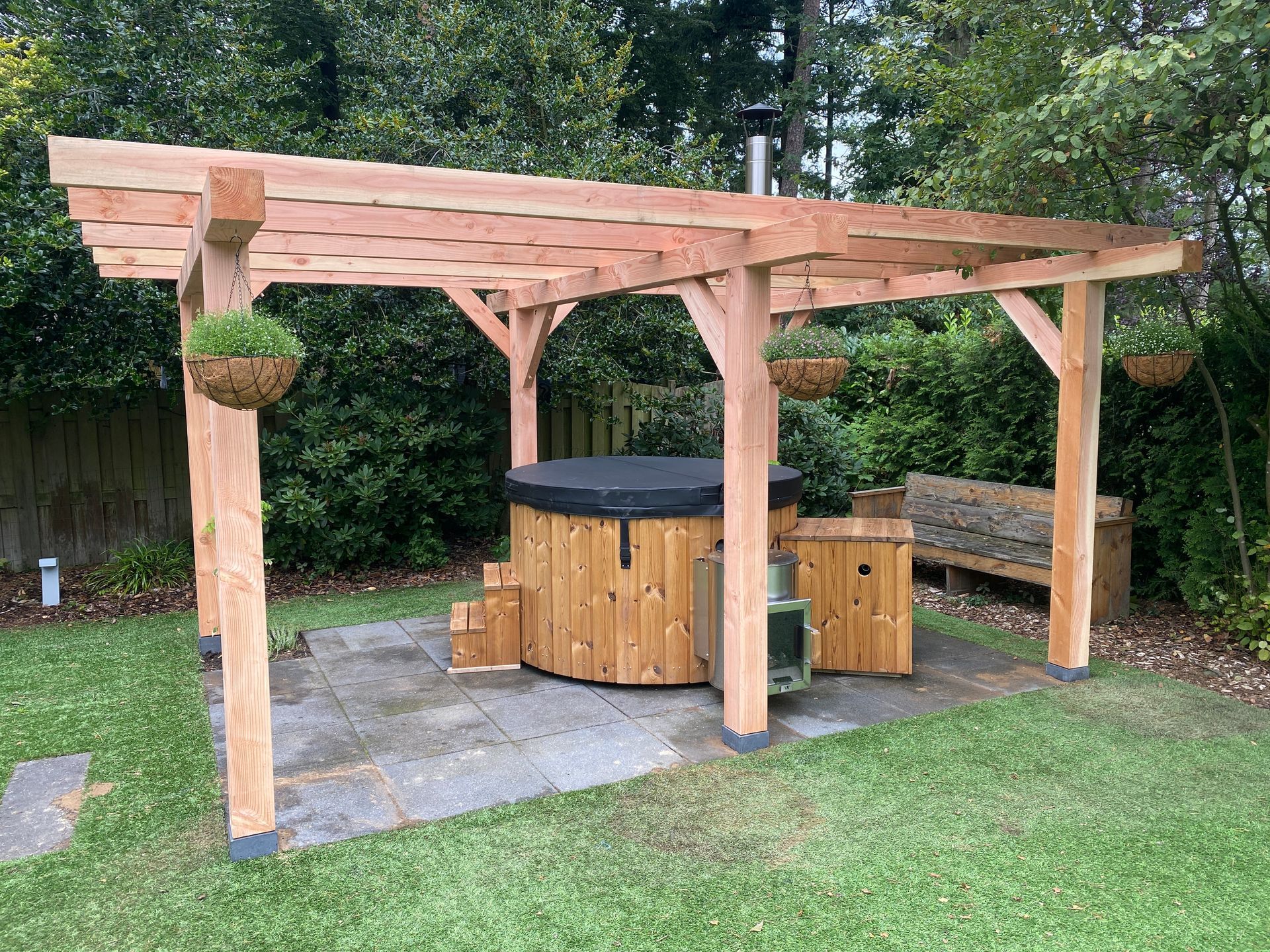 Een houten pergola met een bubbelbad eronder in een achtertuin.