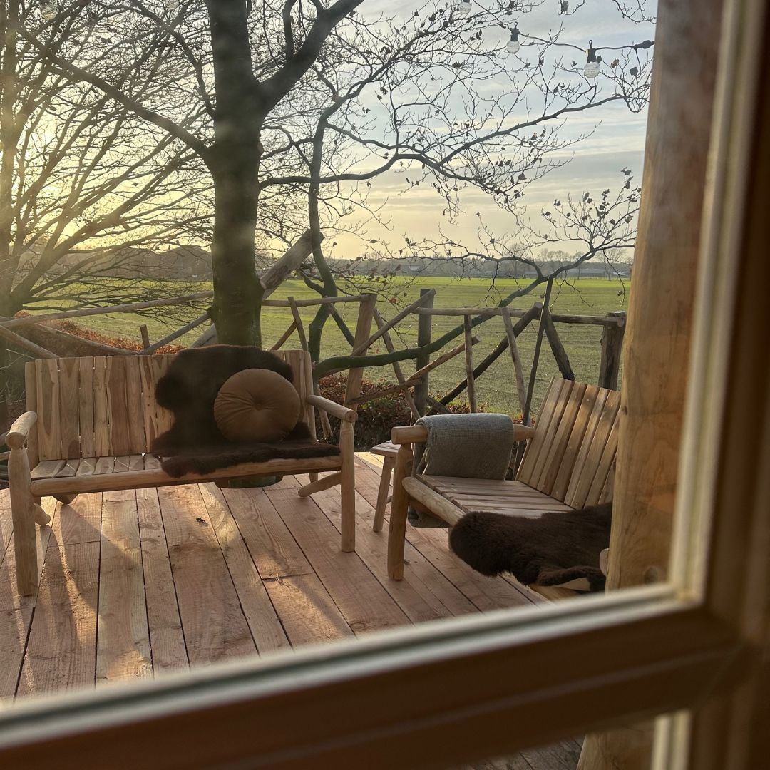 Een houten terras met een bank, stoelen en uitzicht op een veld.