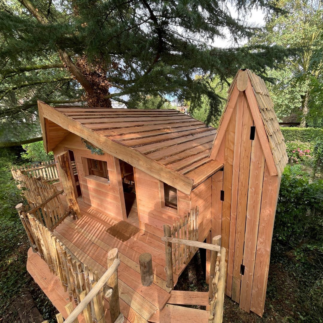 Een houten boomhut met een trap die ernaartoe leidt, staat onder een boom.