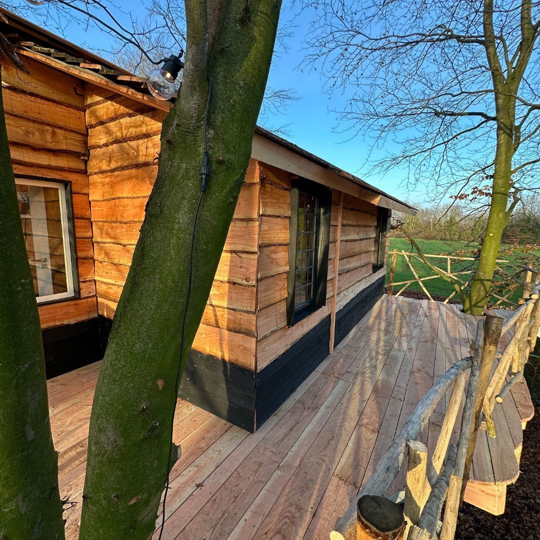 Een houten huis met een terras en bomen ervoor