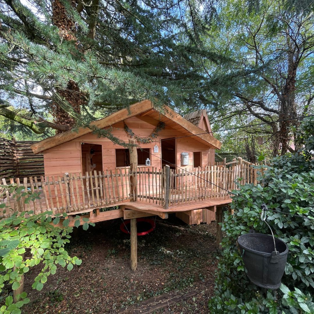 Een houten boomhut staat onder een boom midden in een bos.